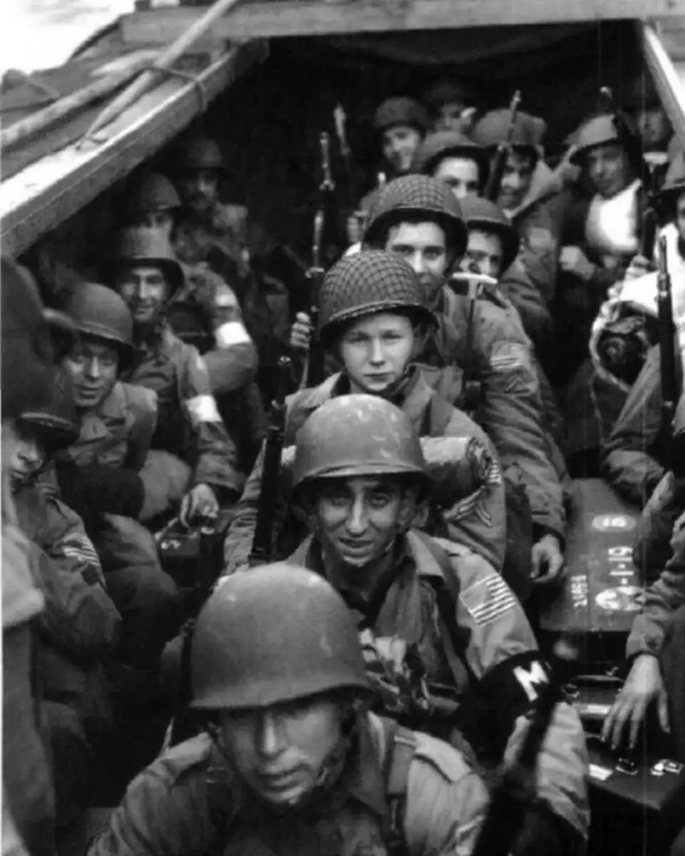 Black and white photo of World War II soldiers in helmets and gear, crowded inside a military landing craft, holding rifles and looking forward, preparing for the D-Day invasion.