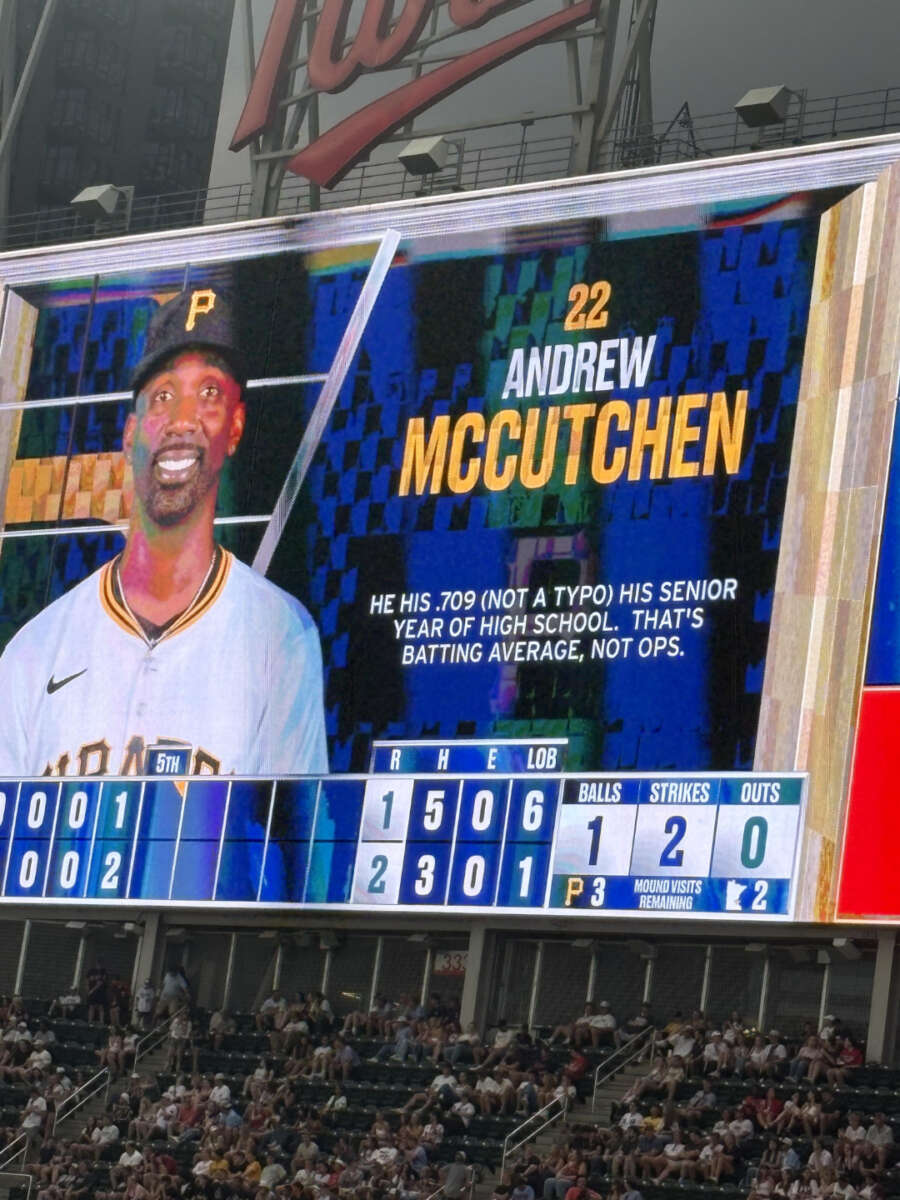 A stadium scoreboard displays Andrew McCutchen (#22) of the Pittsburgh Pirates with a smiling photo and text noting his .709 batting average in high school. Baseball stats and game info are on the screen below.