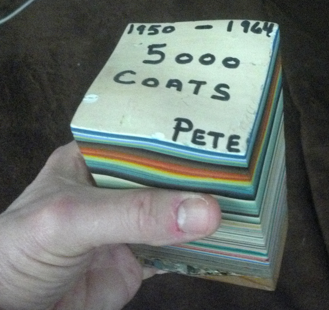 A hand holds a thick block of layered paint chips labeled "1950-1964, 5000 coats, Pete," showing many colorful layers stacked on top of each other.