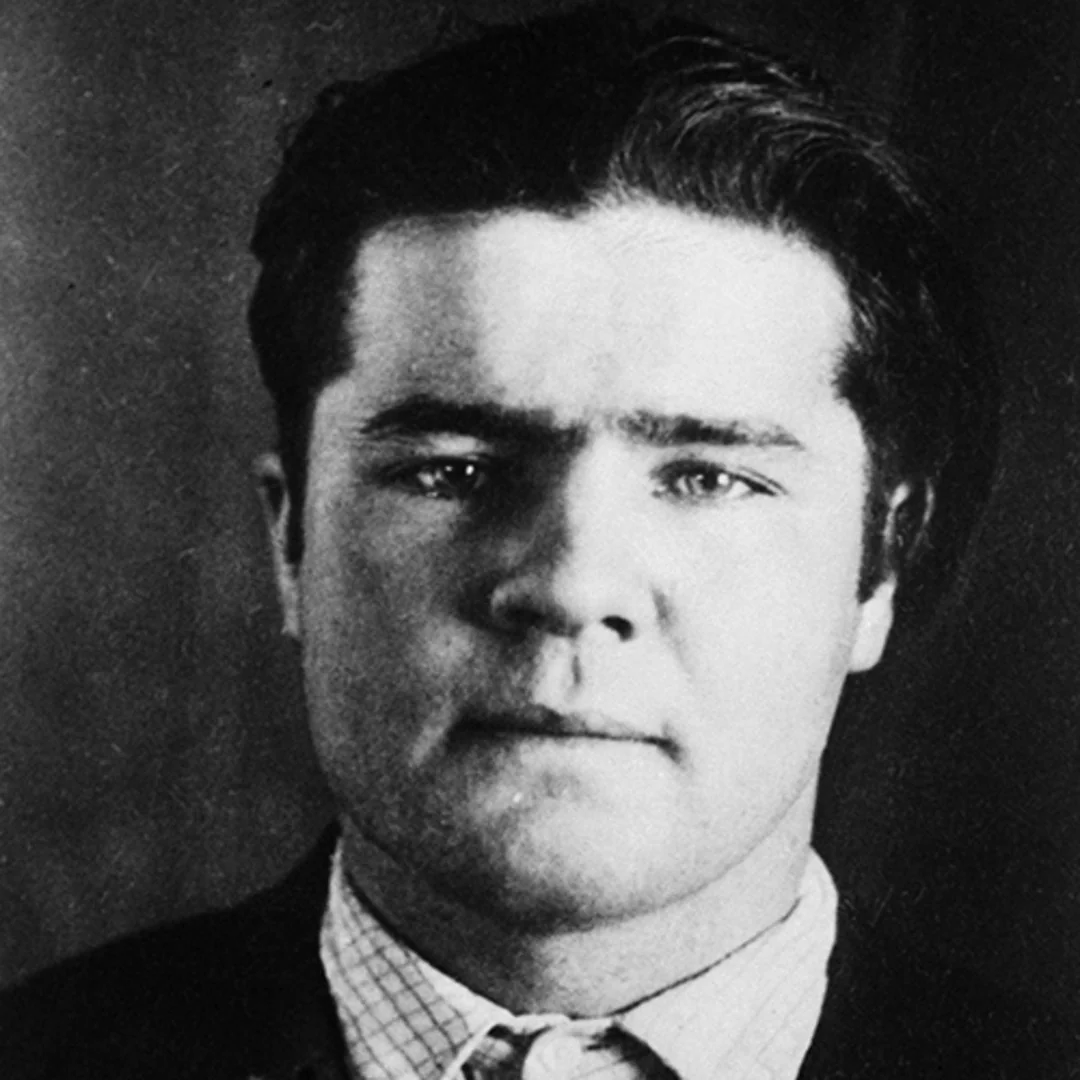 Black and white portrait of a young man with dark hair, wearing a collared shirt and jacket, looking directly at the camera with a neutral expression.