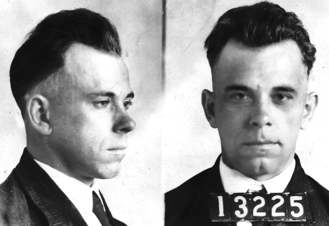 Black and white mugshot of a man with short dark hair, wearing a suit and tie. The left side shows his profile and the right side shows his face with the number 13225 on a placard below.