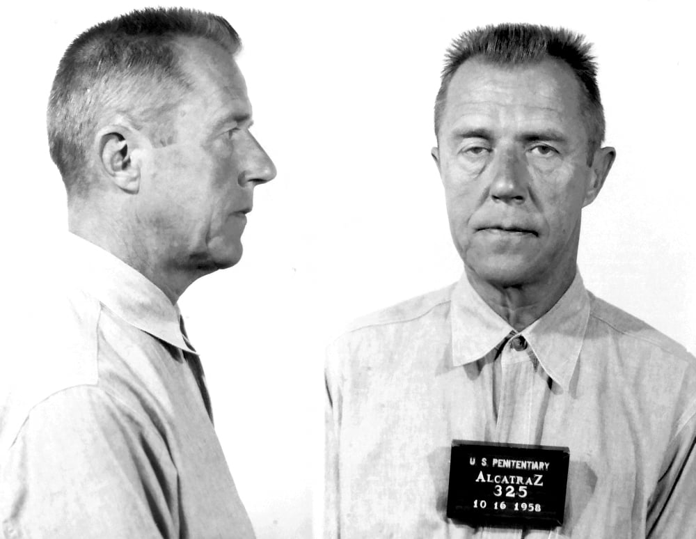 Black and white mugshot of a man in a prison uniform. The photo shows both a side profile and a front view. He holds a sign reading "U.S. Penitentiary Alcatraz 325, 10-16-1958.