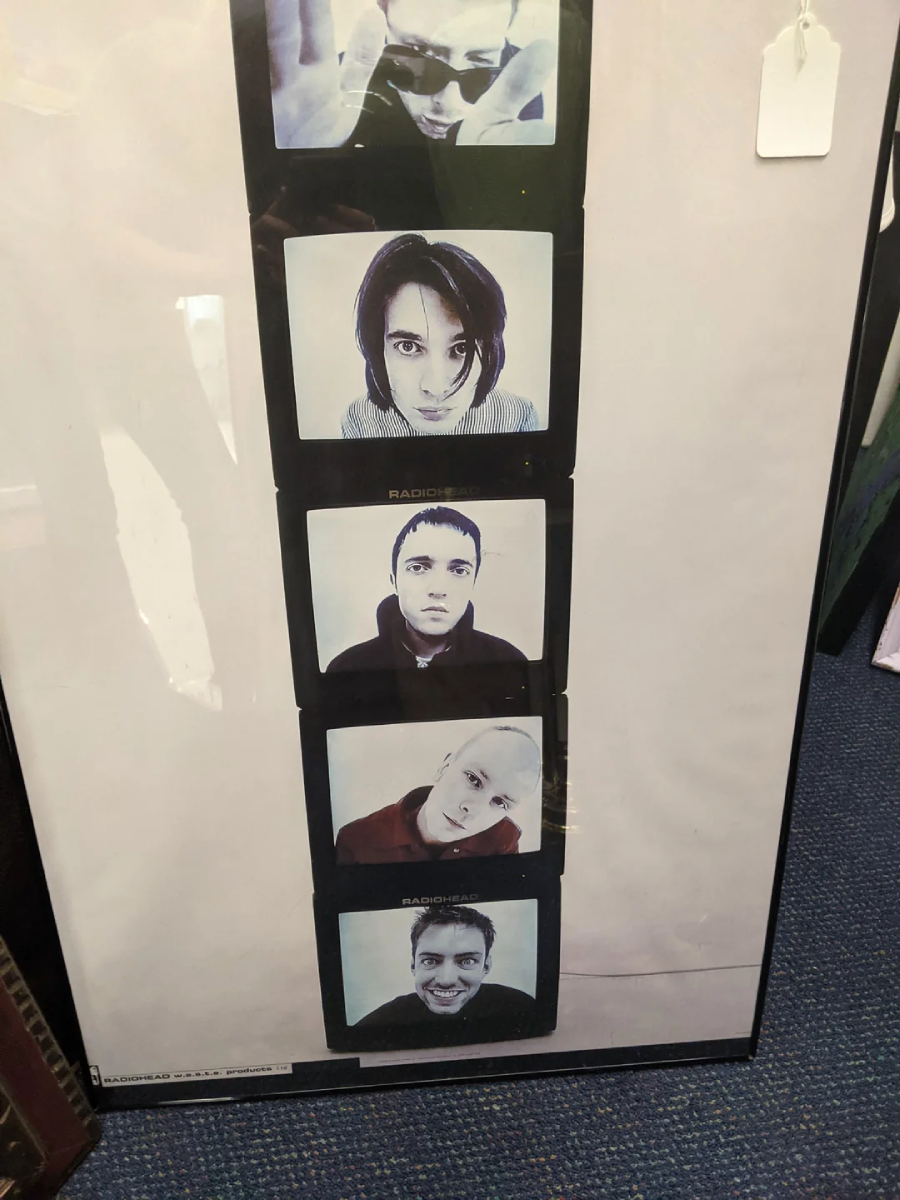 Framed photo strip with five close-up portrait shots of different people, each in a square frame, stacked vertically against a light background. A price tag hangs from the top right corner of the frame.