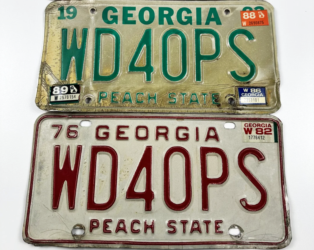Two vintage Georgia license plates with the call sign "WD4OPS," one green and white with 1988 and 1989 stickers, and one red and white with a 1982 sticker. Both read "PEACH STATE" at the bottom.