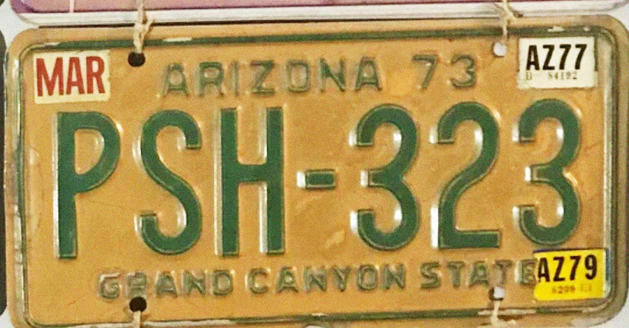 A vintage 1973 Arizona license plate with green text "PSH-323" and "GRAND CANYON STATE" at the bottom. Month sticker reads "MAR" and year stickers for 1977 and 1979 are attached.