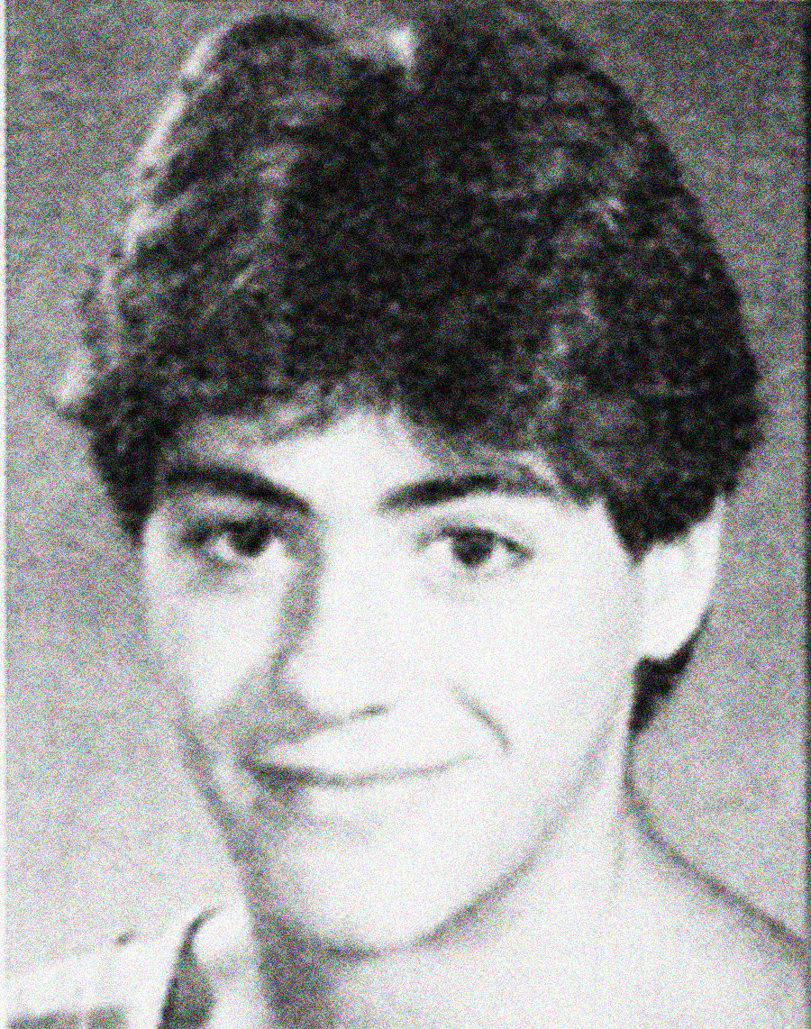 Black and white yearbook-style portrait of a young person with short, dark, wavy hair, smiling softly and looking slightly to the side, against a plain background.