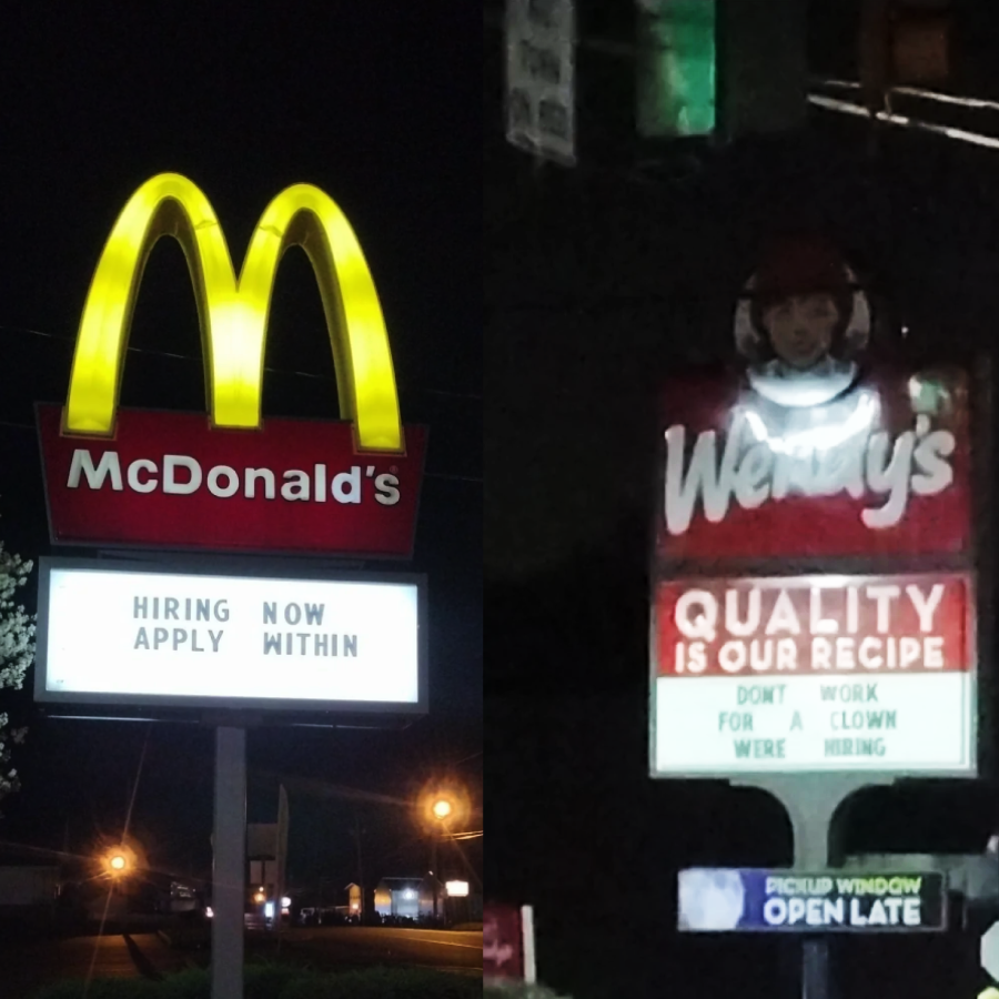 A McDonald's sign reads "HIRING NOW APPLY WITHIN" next to a Wendy's sign that says "QUALITY IS OUR RECIPE" with rearranged letters spelling "DON'T WORK FOR CLOWN, WE'RE HIRING" underneath. Both signs are lit at night.