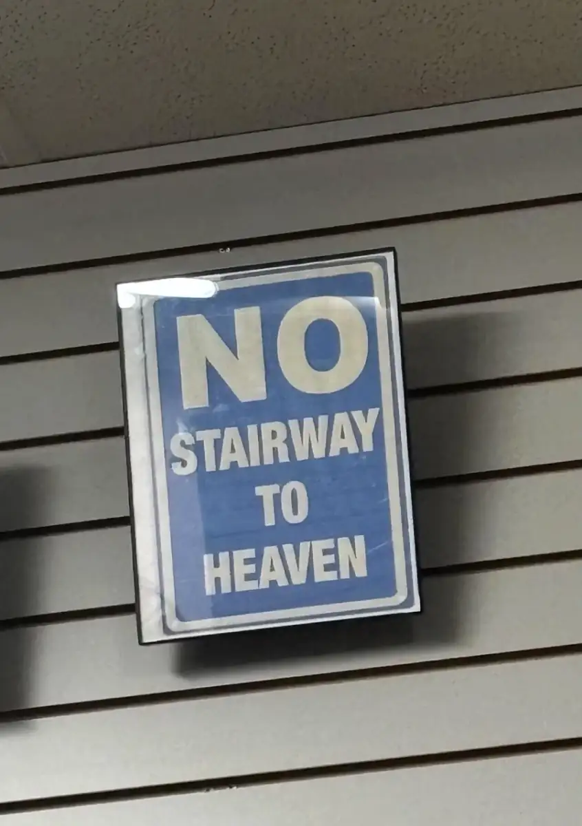 A blue and white sign on a wall reads, "NO STAIRWAY TO HEAVEN" in bold letters, referencing the famous Led Zeppelin song.