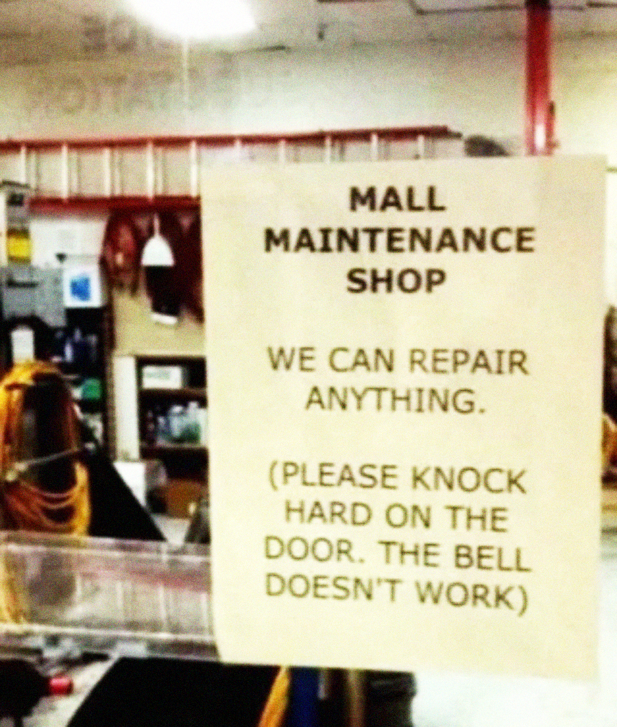 A sign in a maintenance shop reads: "Mall Maintenance Shop. We can repair anything. (Please knock hard on the door. The bell doesn't work)." Various tools and equipment are visible in the background.