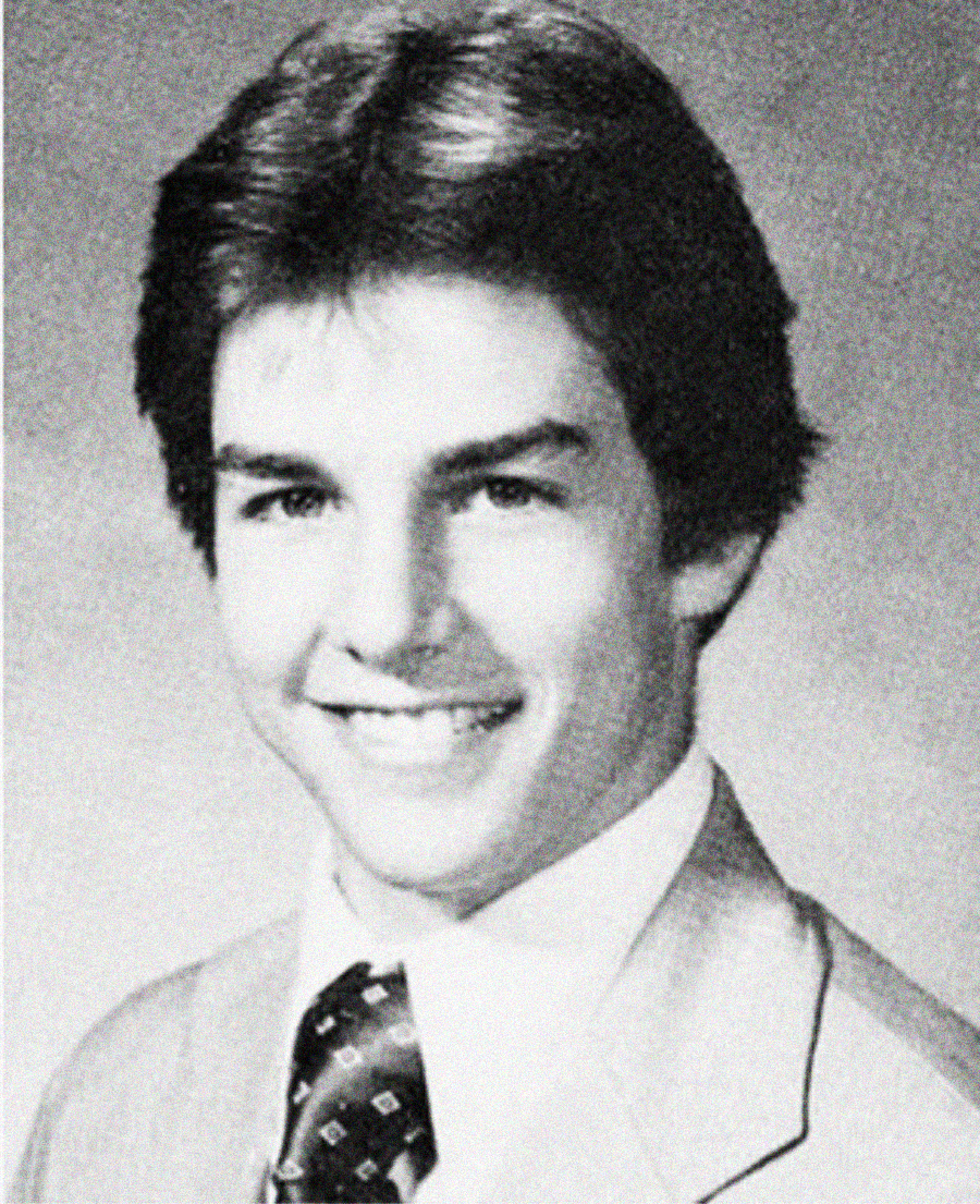 Black and white portrait of a young man with short, dark hair, smiling and wearing a light-colored suit jacket, white shirt, and patterned tie. The photo has a classic yearbook style.
