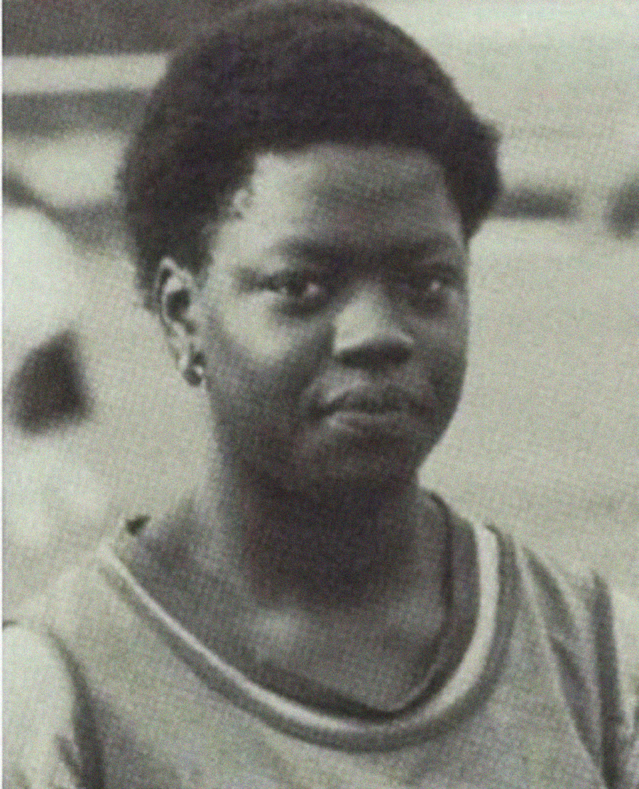Black and white photo of a person with short hair, wearing a sleeveless top, looking directly at the camera with a neutral expression.