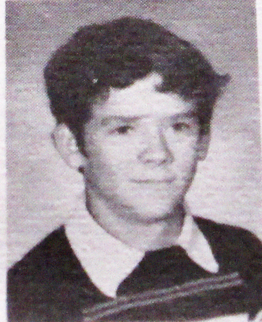 Black and white yearbook photo of a young person with short, dark wavy hair, wearing a collared shirt under a sweater, looking slightly to the side with a neutral expression.