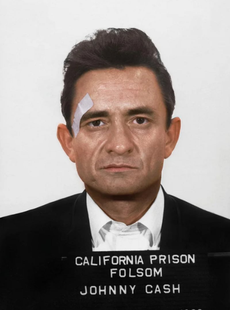 A man in a suit with a bandage on his forehead poses for a mugshot against a plain background. The sign reads "California Prison Folsom Johnny Cash.