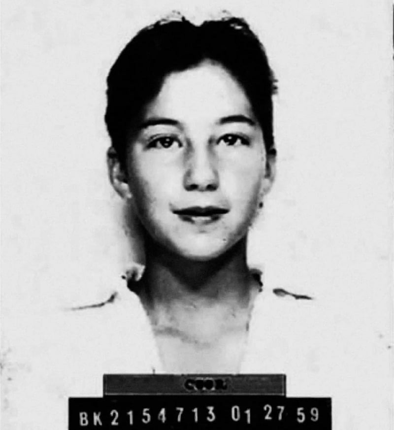 Black and white mugshot of a young woman with short dark hair, wearing a light-colored shirt, looking straight at the camera. A placard with identification numbers is visible at the bottom.