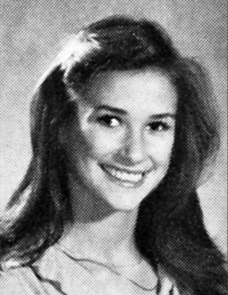 Black and white yearbook-style portrait of a young woman with long, dark hair, smiling, looking slightly to the side, and wearing a light-colored top. The background is plain and softly lit.