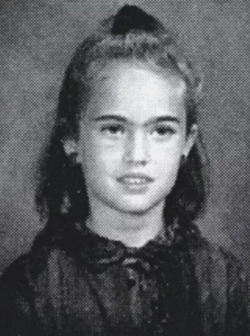 Black and white yearbook-style portrait of a young girl with dark, shoulder-length hair pulled back in a ponytail, wearing a collared top and looking at the camera with a neutral expression.