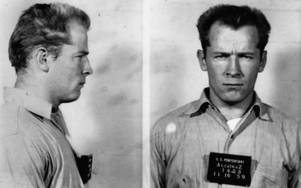 Black-and-white mugshot of a stern-looking man facing left in the side view and forward in the front view, wearing a collared shirt with an identification tag reading "Alcatraz" on his chest.