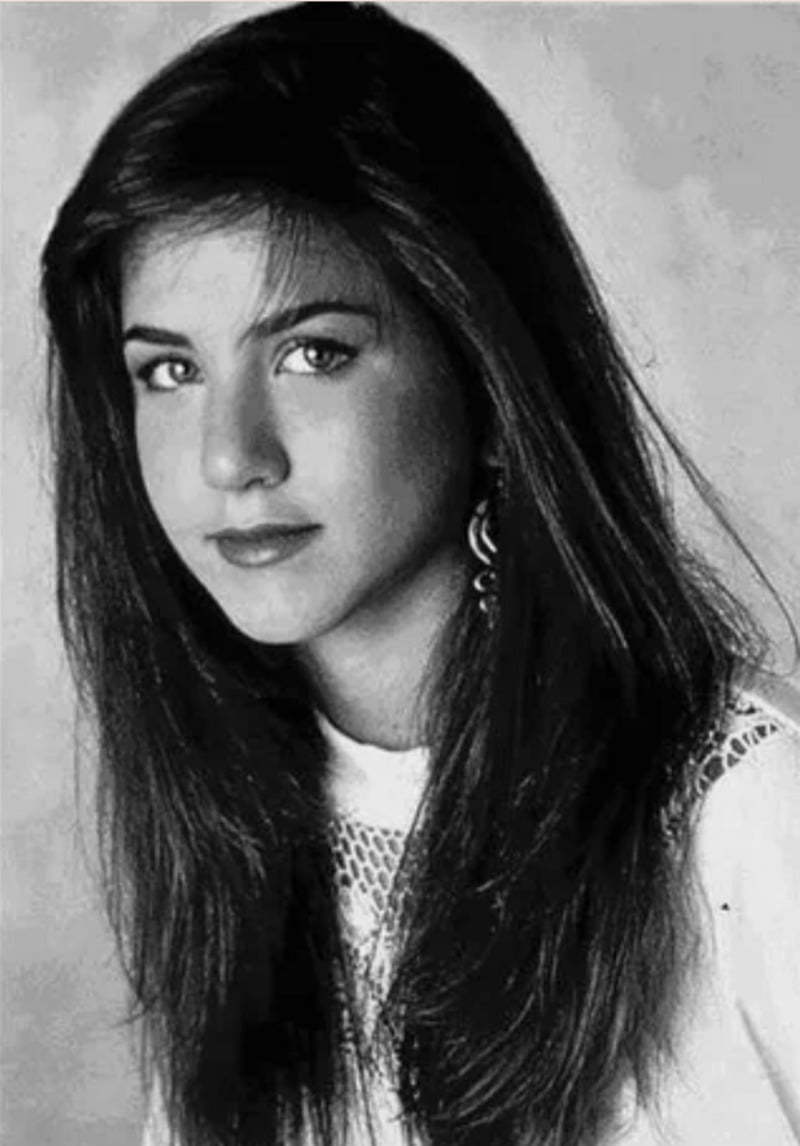 A young woman with long, straight dark hair and light eyes looks slightly to the side. She wears a light-colored top with lace detail, and the photo is in black and white.