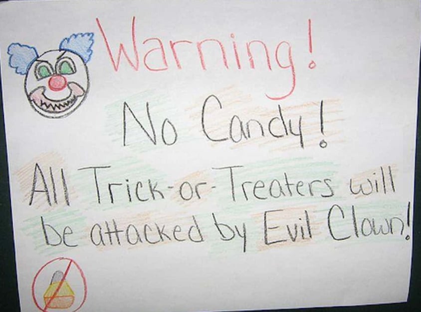 A hand-drawn sign with a clown face and red text reads, "Warning! No Candy! All Trick-or-Treaters will be attacked by Evil Clown!" with a crossed-out candy symbol in the corner.