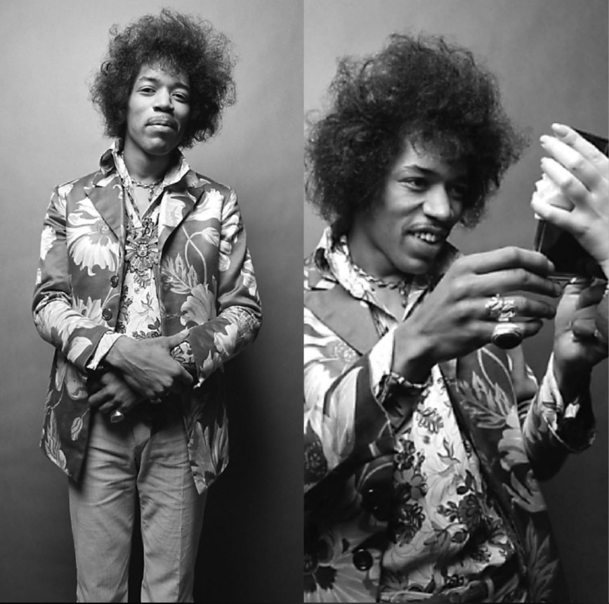 Black and white photos of a man with curly hair wearing a patterned shirt and floral jacket; in one image he stands with arms crossed, in the other he looks at an object being handed to him.