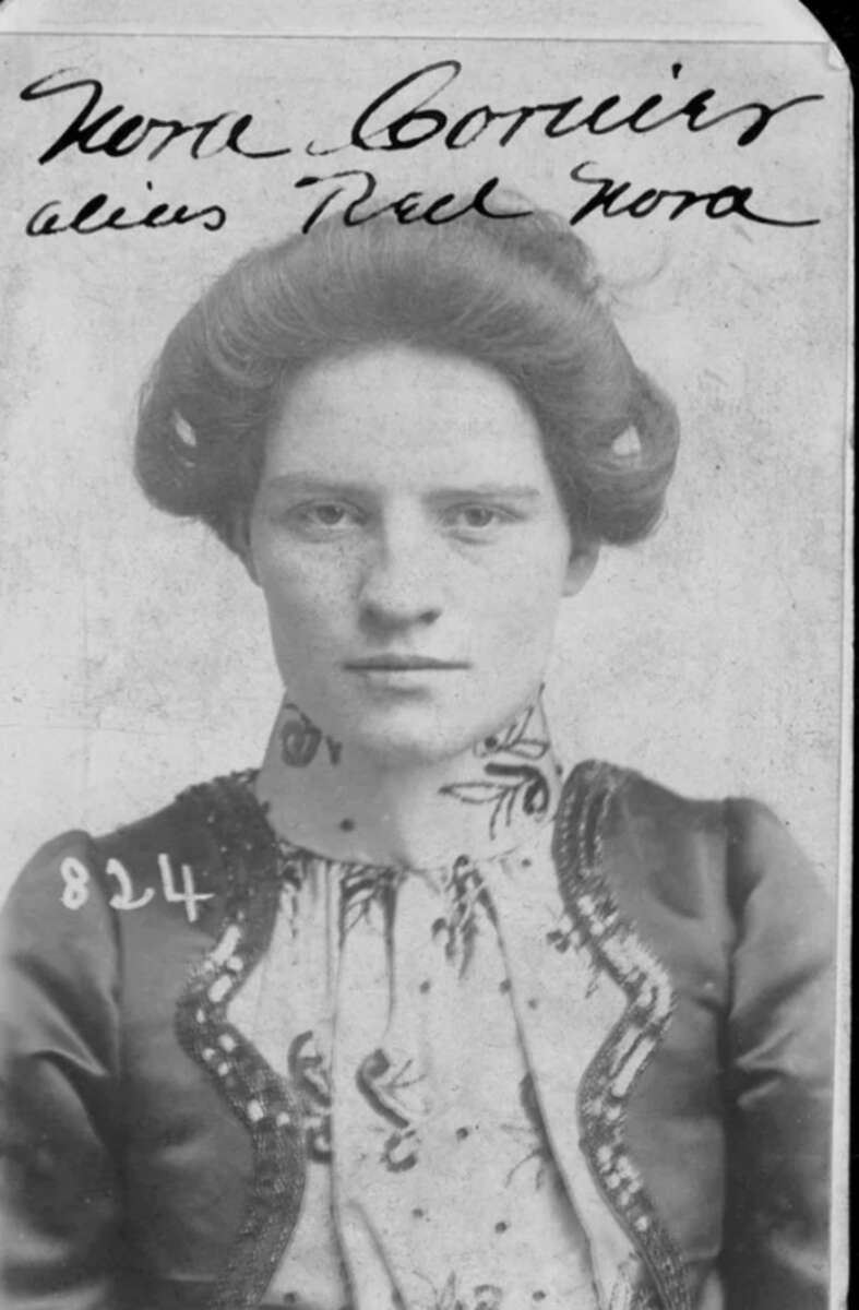 Black-and-white portrait of a young woman with an elaborate updo hairstyle, wearing a patterned, high-collared blouse and dark jacket. Handwritten text and numbers appear above and on her image.