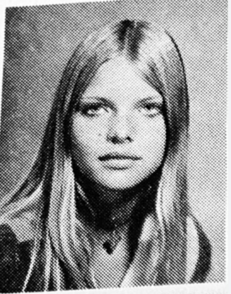 Black-and-white, grainy yearbook-style portrait of a young woman with long straight hair, center-parted, looking directly at the camera with a neutral expression, wearing a necklace.