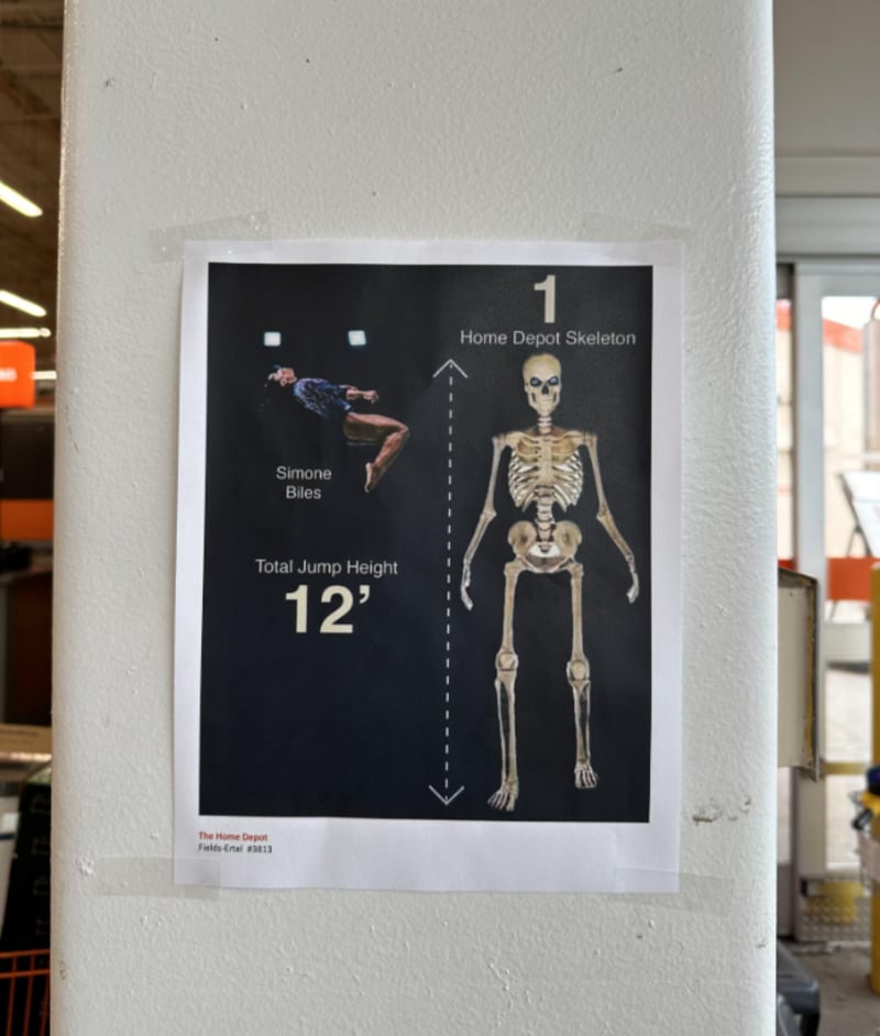 A poster compares Simone Biles, shown mid-flip, with a Home Depot skeleton. It notes Biles’ total jump height as 12 feet, matching the skeleton’s height, with arrows indicating the measurement.