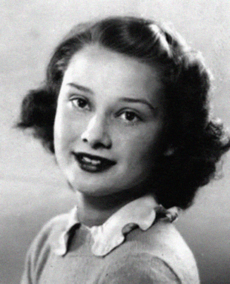 Black and white portrait of a young girl with wavy dark hair, wearing a light-colored top with a scalloped white collar, smiling slightly and looking towards the camera against a plain background.