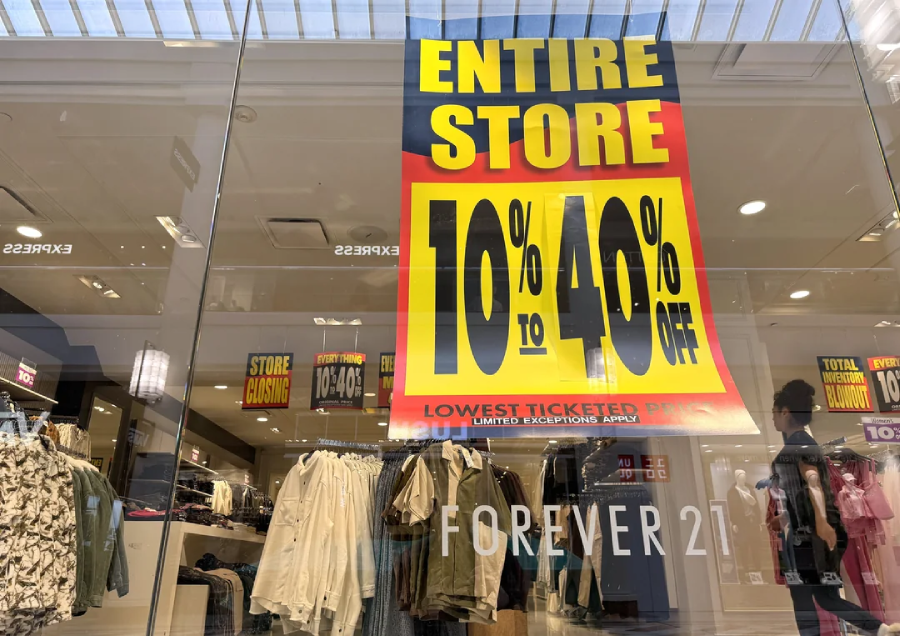 A large sign in a Forever 21 store window advertises “ENTIRE STORE 10% to 40% OFF” in bold letters. The sign reflects the mall interior, and mannequins display clothes inside the store.