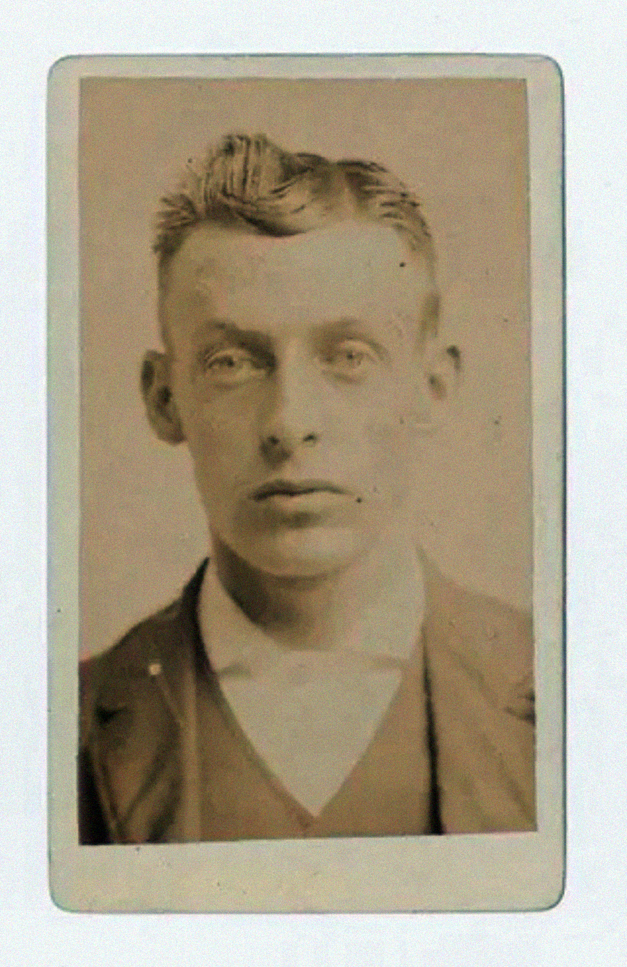A sepia-toned vintage portrait of a young man with short, neatly combed hair, wearing a suit jacket, vest, and white shirt, facing forward with a neutral expression. The photo has an old, faded appearance.