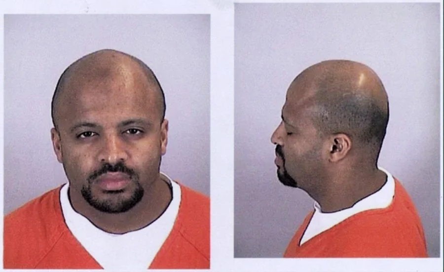 Mugshot of a man in an orange prison uniform, shown from the front and side against a plain background. He has a bald head, trimmed beard, and neutral expression.