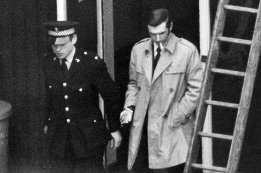 A man in a trench coat and a police officer in a doorway