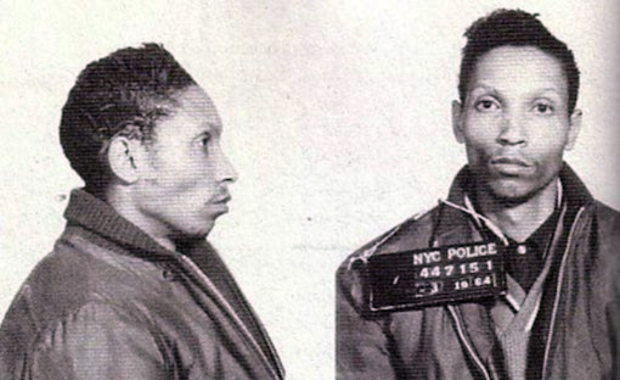 Black and white mugshot showing a man facing forward and in profile, wearing a jacket, with a NYC Police placard around his neck displaying numbers and the year 1964.