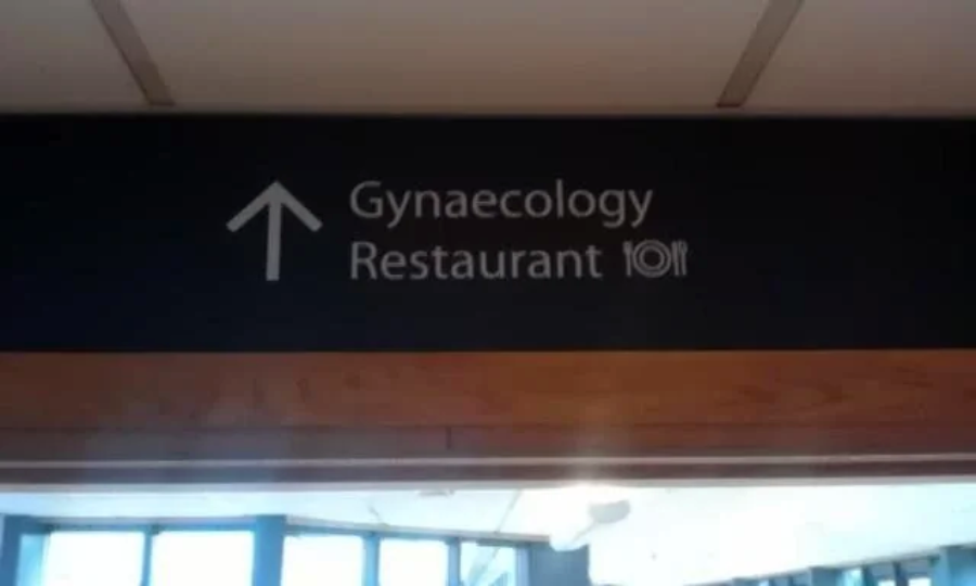 A sign above a doorway points straight ahead to "Gynaecology" and "Restaurant," with a plate and cutlery icon next to "Restaurant," creating an amusing and confusing combination.