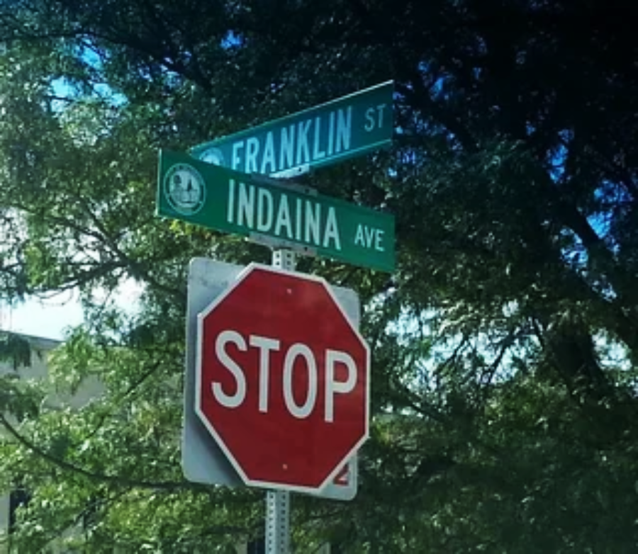 Street signs at an intersection show "Franklin St" and "Indaina Ave," with a "Stop" sign below them. Trees and greenery are visible in the background.
