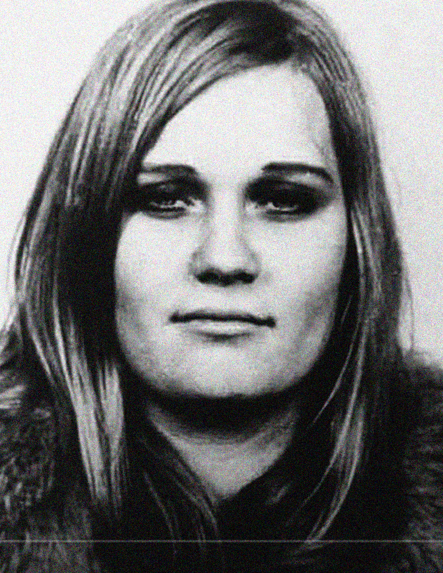 Black and white portrait of a young woman with long, straight hair, wearing a fur-collared coat. She gazes directly at the camera with a neutral expression.