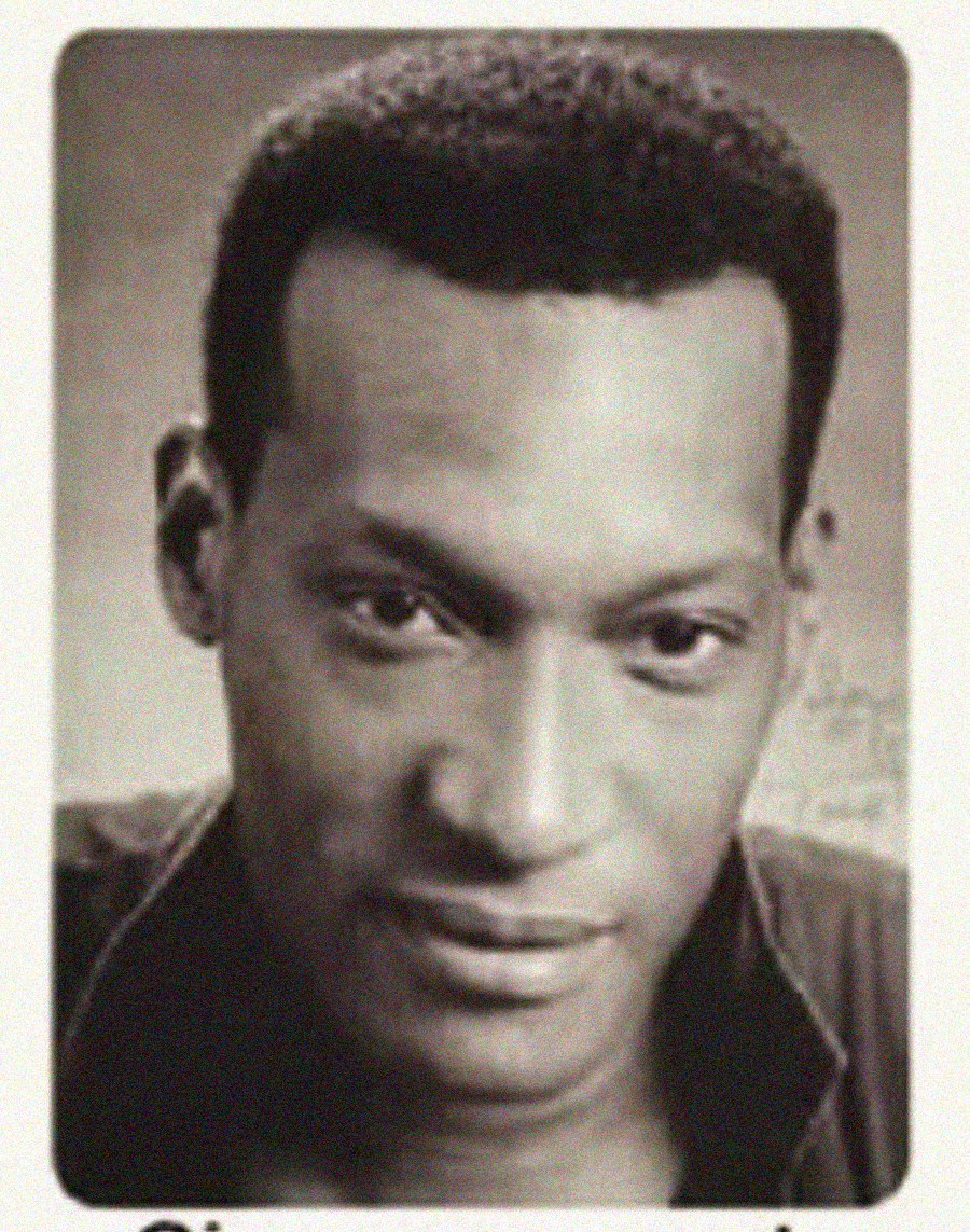 A black and white portrait of a man with short hair, wearing an open-collared shirt, facing the camera with a slight smile.