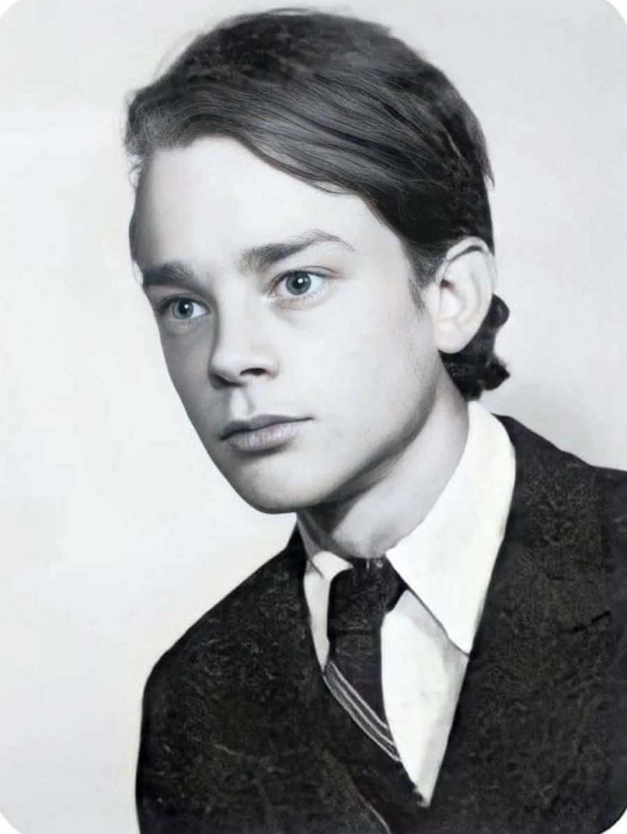 A black-and-white portrait of a young person wearing a suit and tie, with neatly combed hair and a serious expression, looking slightly to the side against a plain background.