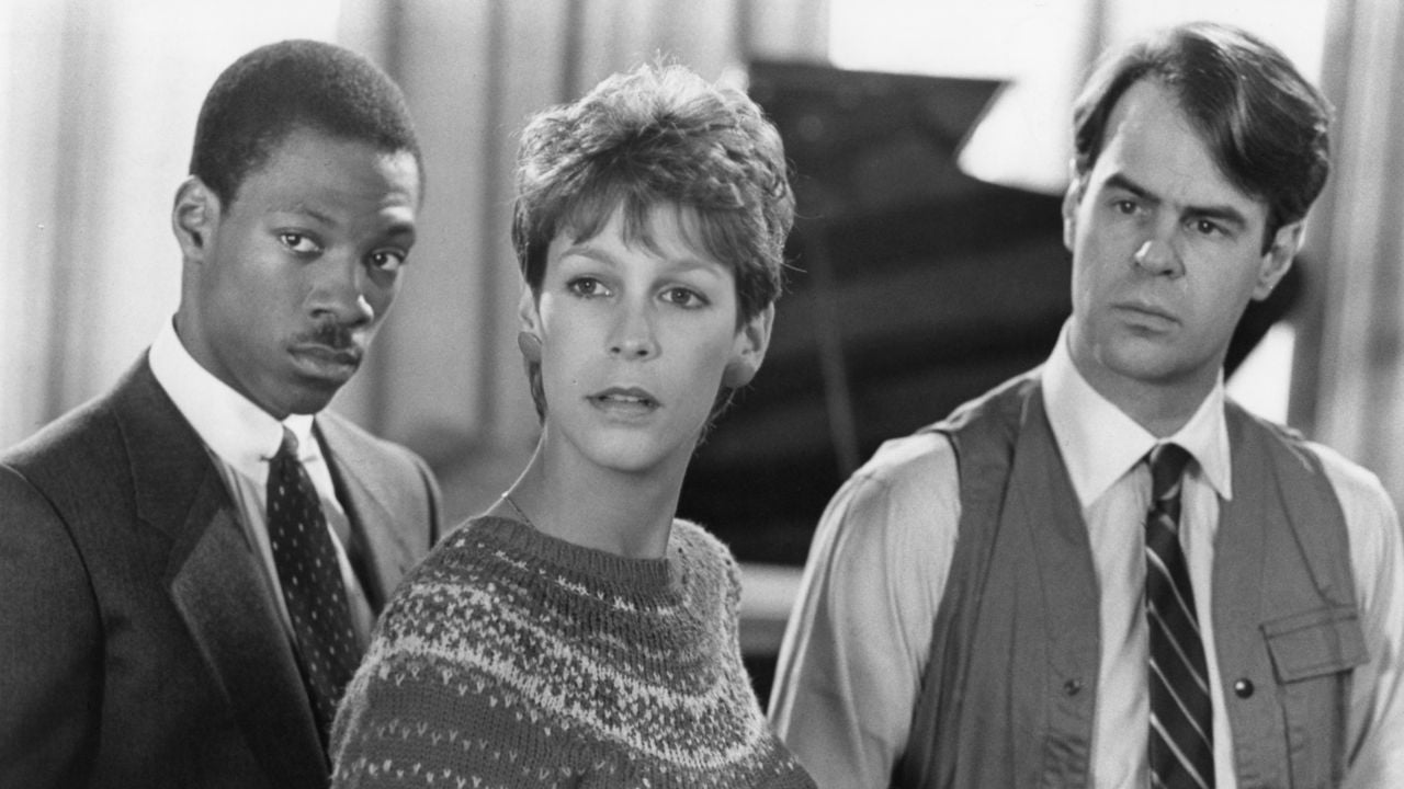 Three people stand close together indoors, looking in the same direction with serious and curious expressions. The setting appears formal, with two in business attire and one in a sweater. The image is black and white.