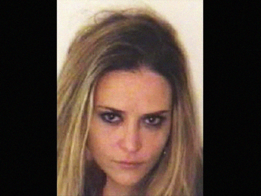 A woman with long, straight, light brown hair stares directly at the camera with a serious expression. The background is plain and light-colored. The image is framed with black bars on the left and right sides.