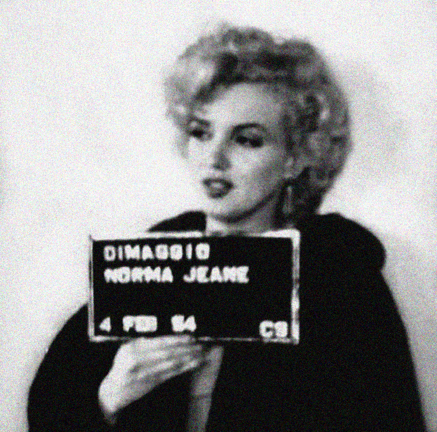 A black and white, grainy photo of a woman with curled blonde hair holding a sign that reads "DiMaggio Norma Jeane 4 Feb 64." She stands against a plain background, wearing a dark garment.