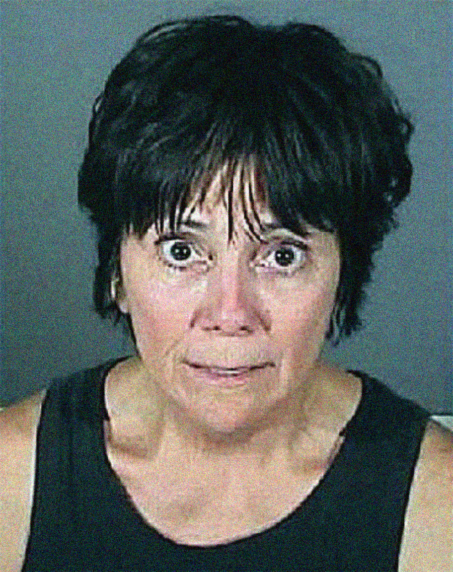 A woman with short dark hair wearing a black sleeveless top looks directly at the camera with a serious and concerned expression against a plain gray background.