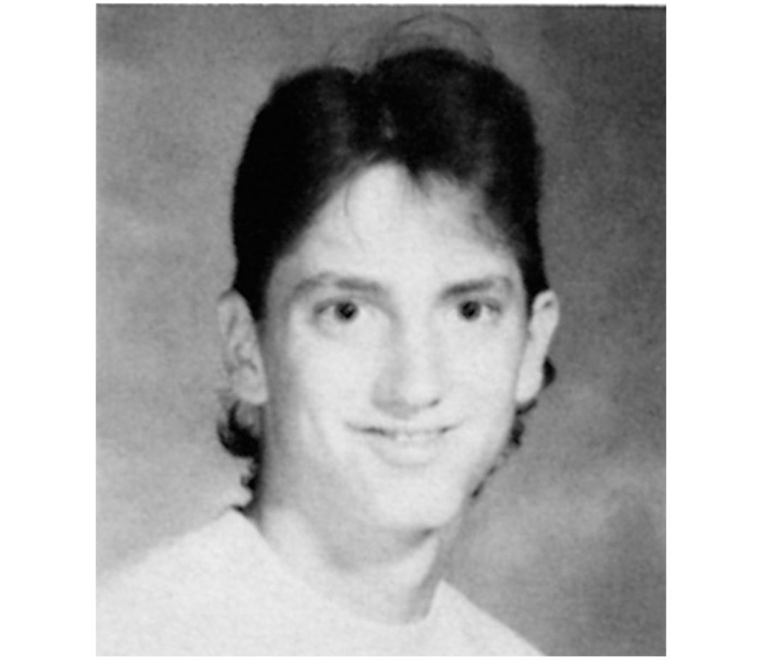 Black and white yearbook-style portrait of a young person with short, dark hair, wearing a light-colored shirt, smiling and looking at the camera. The background is plain and softly blurred.