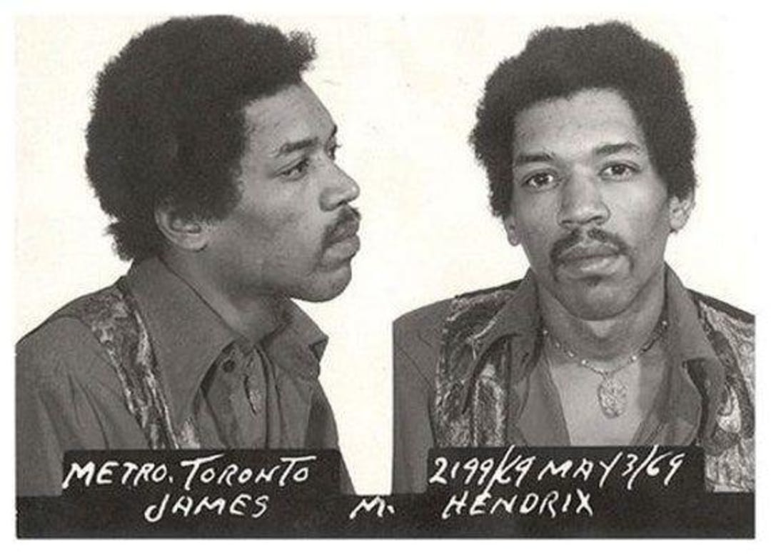 Black-and-white mugshot of a man with an afro, wearing a patterned shirt and necklace. Text beneath reads "METRO. TORONTO JAMES" and "2199K9 MAY 3/69 M. HENDRIX".