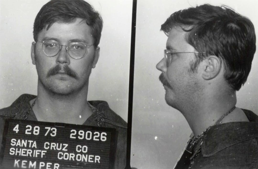 Black and white mugshot of a man with short hair, mustache, and glasses. He is shown from the front and side, holding a board that reads “Santa Cruz Co Sheriff Coroner Kemper 4 28 73 29026.”