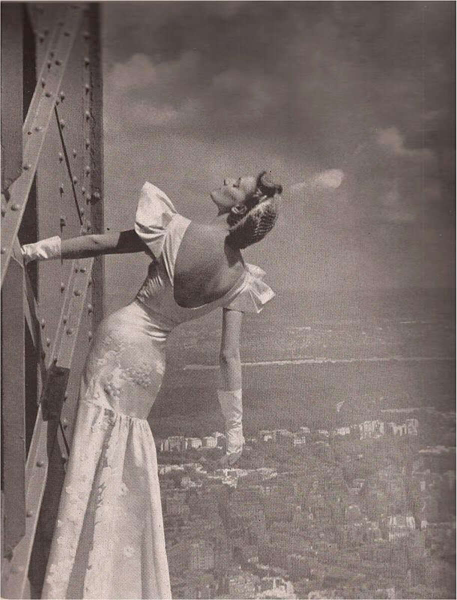 A woman in a dress leaning on a metal structure