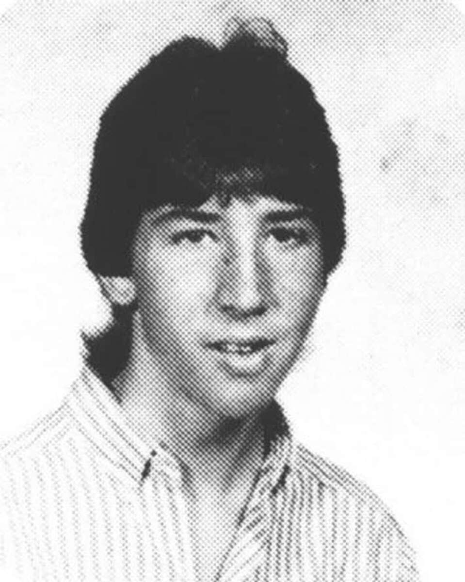 Black and white yearbook-style photo of a teenage boy with medium-length dark hair, wearing a striped button-down shirt, looking at the camera with a neutral expression.