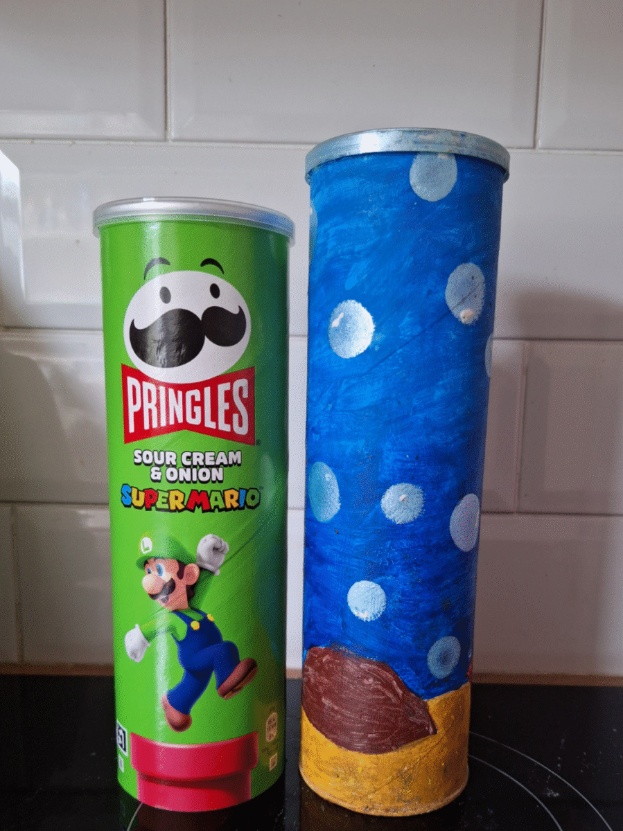 A Pringles Sour Cream & Onion can with Super Mario graphics stands next to a similar-sized can painted blue with white spots and a brown patch, resembling a Super Mario mushroom. Both cans are placed on a kitchen counter.