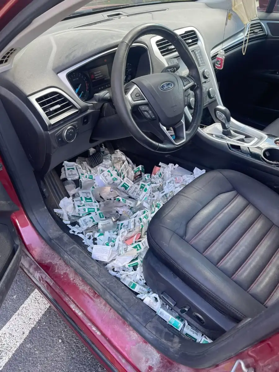 The interior of a red Ford car with the front door open, showing the floor on the driver's side covered in numerous single-serve condiment packets, mostly ketchup and other sauces.