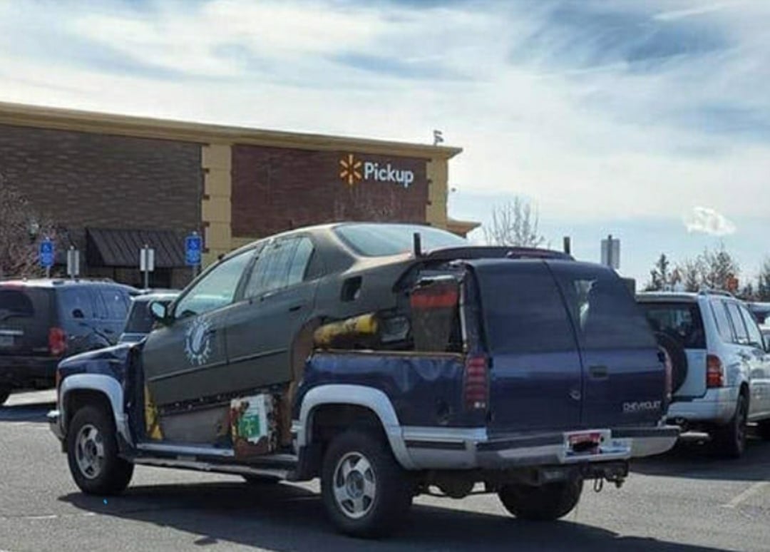 A car is humorously fused with a pickup truck, creating a mismatched vehicle parked outside a Walmart with a "Pickup" sign visible on the building. Other cars are parked nearby under a partly cloudy sky.